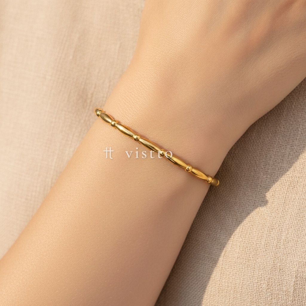 Pulsera dorada fina y abierta, diseño de brazalete de piezas ovaladas unidas por pequeñas bolitas y acabado brillante