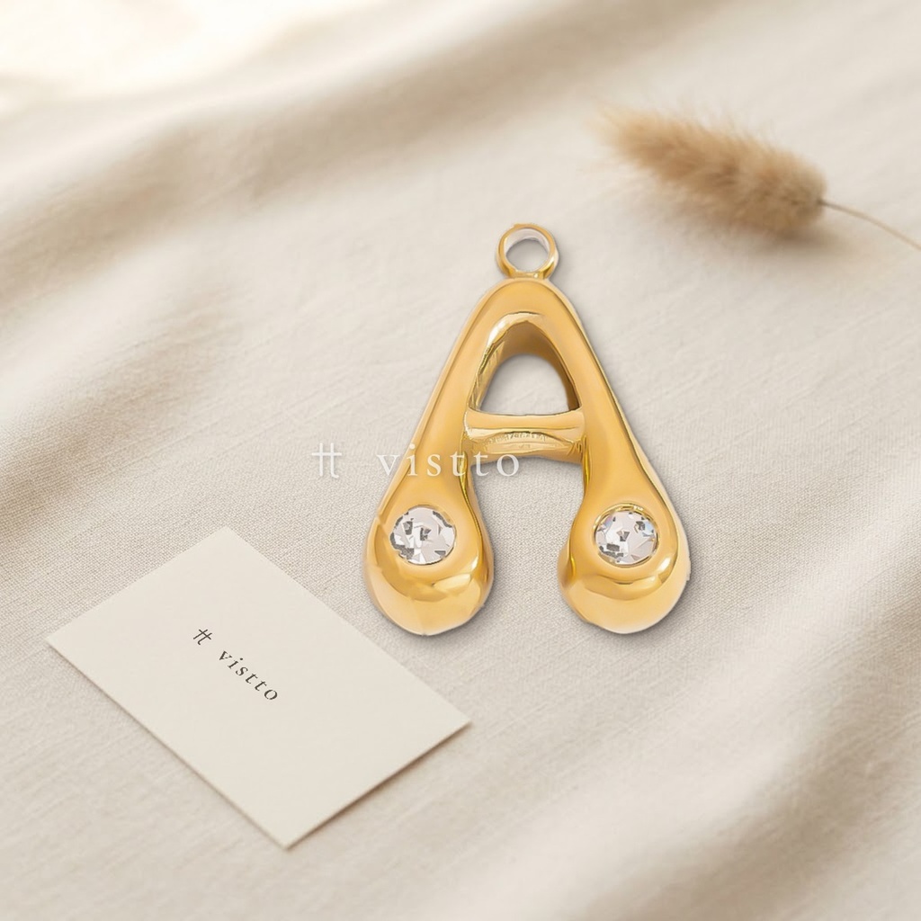 Dije dorado en forma de letra A de trazo abombado y liso, con circonias transparentes en los extremos y argolla superior