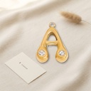 Dije dorado en forma de letra A de trazo abombado y liso, con circonias transparentes en los extremos y argolla superior
