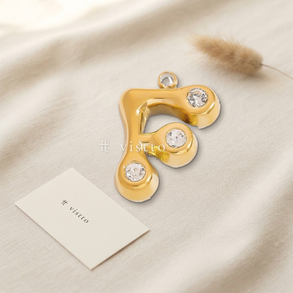 Dije dorado en forma de letra F de trazo abombado y liso, con circonias transparentes en los extremos y argolla superior