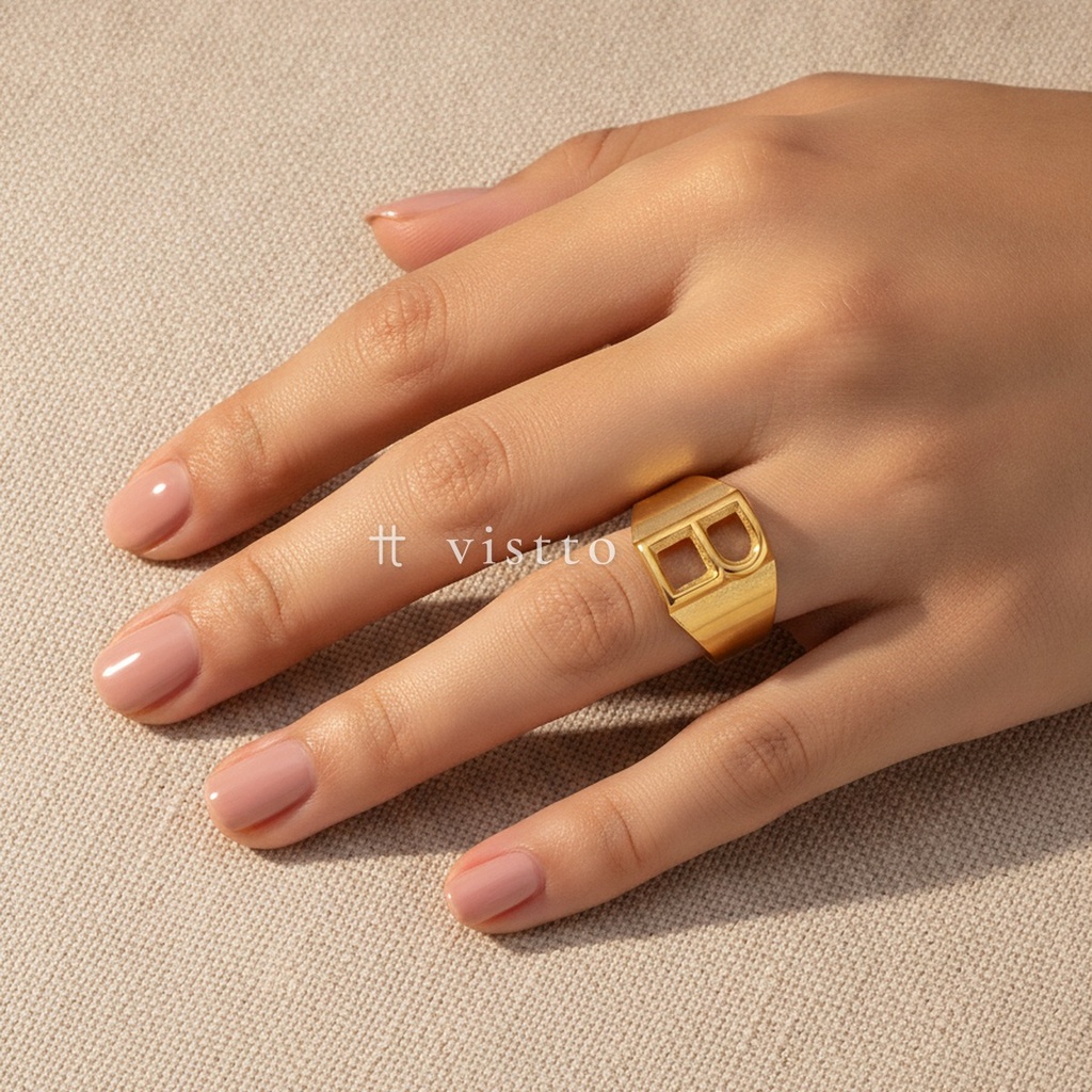 Anillo dorado ancho y abierto, diseño de banda lisa con motivo frontal de la letra B calada y acabado brillante