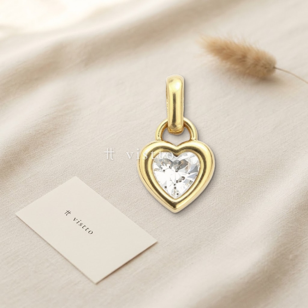 Dije dorado en forma de corazón con borde liso, una circonia transparente en talla corazón y anilla para colgar
